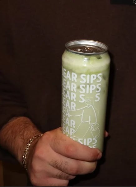Hand holding a pale green canned beverage labeled Sips against a dark background
