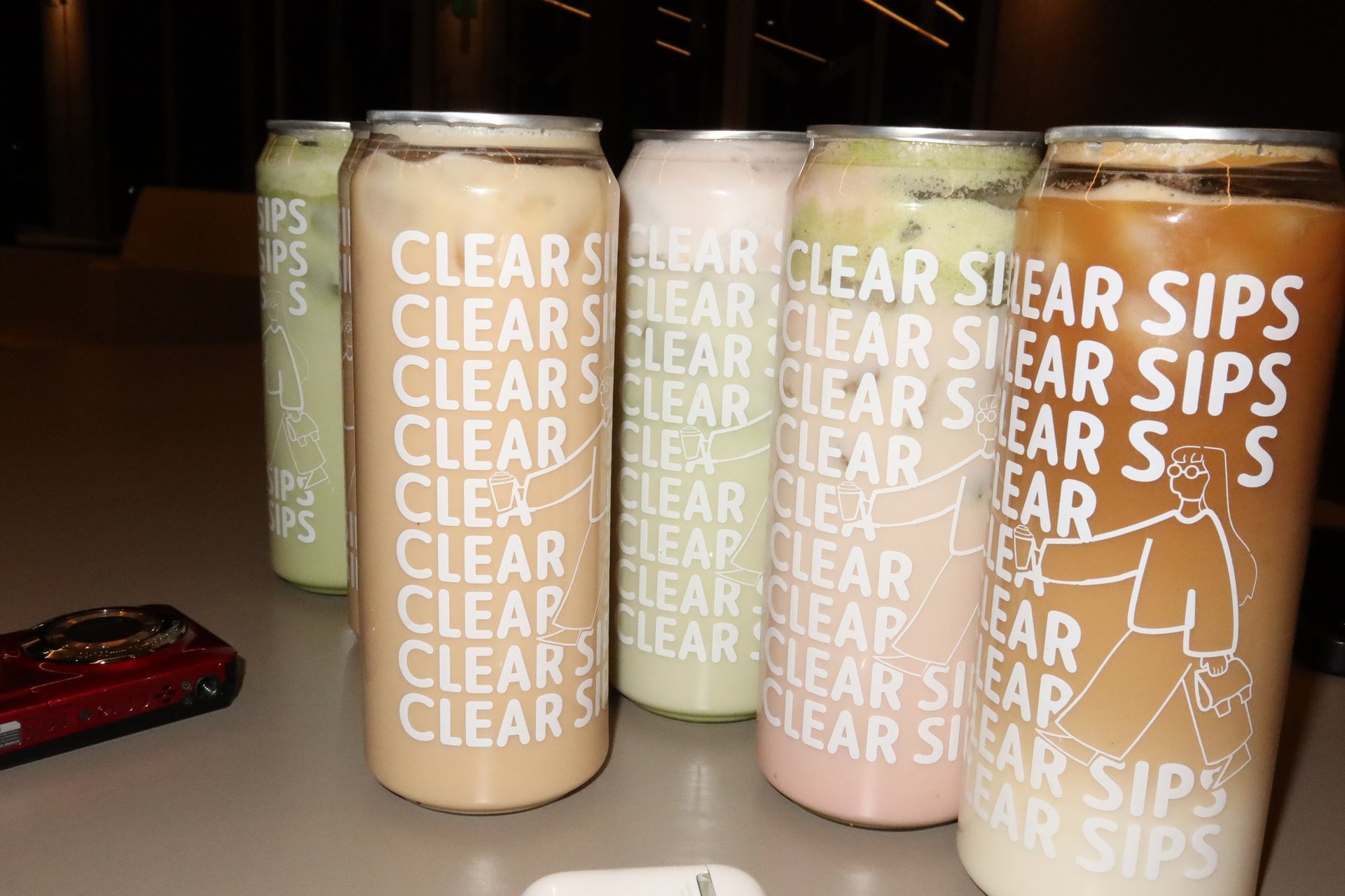 Five cans of Clear Sips beverage in different pastel colors arranged in a row on a table